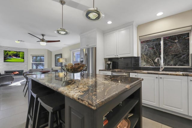 kitchen featuring white cabinets, a large fireplace, dark stone counters, and stainless steel fridge