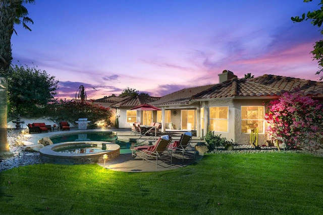 back house at dusk with a patio area, a swimming pool with hot tub, and a lawn