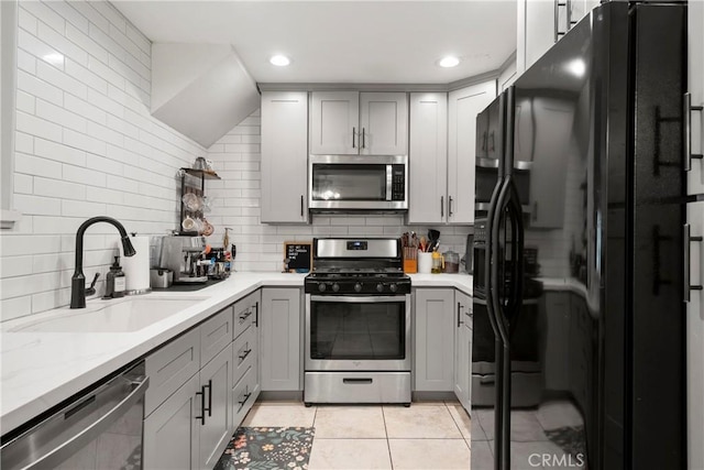 kitchen featuring appliances with stainless steel finishes, gray cabinetry, light tile patterned floors, decorative backsplash, and sink