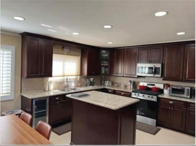 kitchen with sink, light stone counters, dark brown cabinets, a kitchen island, and stainless steel appliances