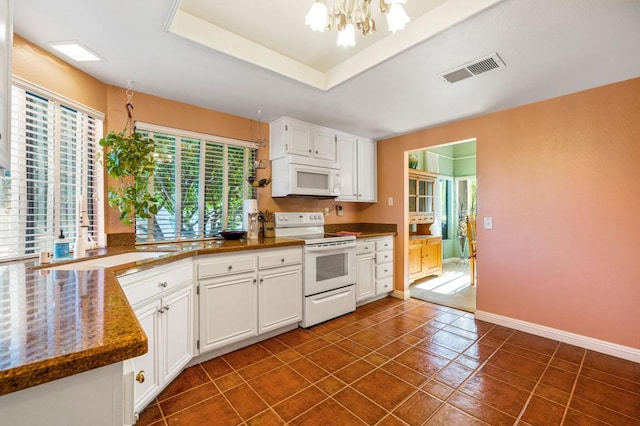 kitchen featuring white cabinets, an inviting chandelier, white appliances, dark tile patterned floors, and a tray ceiling