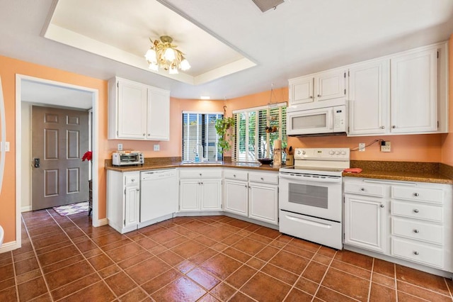 kitchen with white appliances, dark tile patterned floors, a tray ceiling, white cabinets, and sink