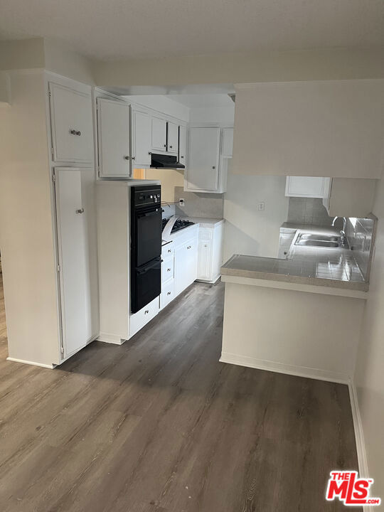 kitchen with kitchen peninsula, dark hardwood / wood-style floors, white cabinetry, double oven, and sink