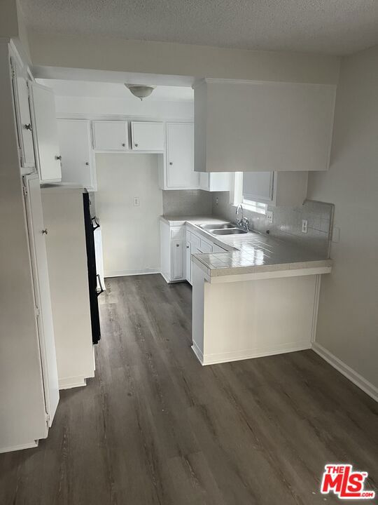 kitchen featuring kitchen peninsula, a textured ceiling, dark wood-type flooring, sink, and white cabinetry