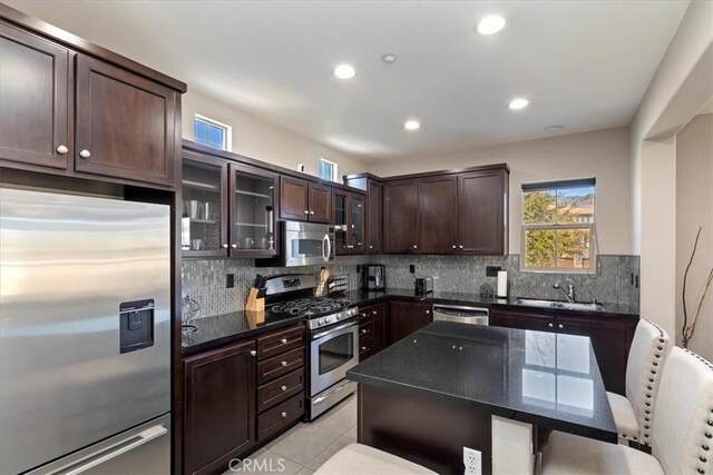 kitchen with a kitchen breakfast bar, stainless steel appliances, light tile patterned floors, decorative backsplash, and sink