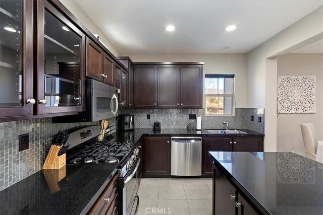 kitchen featuring sink, light tile patterned floors, backsplash, dark brown cabinetry, and appliances with stainless steel finishes