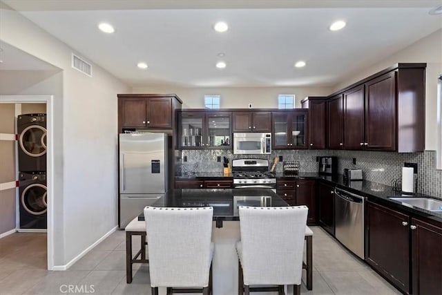 kitchen with light tile patterned floors, stacked washer and clothes dryer, a kitchen island, a breakfast bar, and appliances with stainless steel finishes