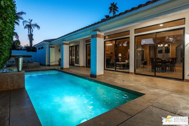 pool at dusk featuring a jacuzzi and a patio