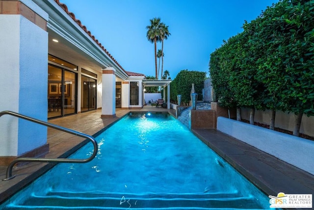 pool at dusk featuring a patio, pool water feature, and a pergola