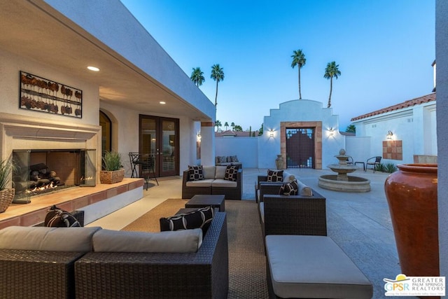 patio terrace at dusk featuring french doors and an outdoor living space with a fireplace