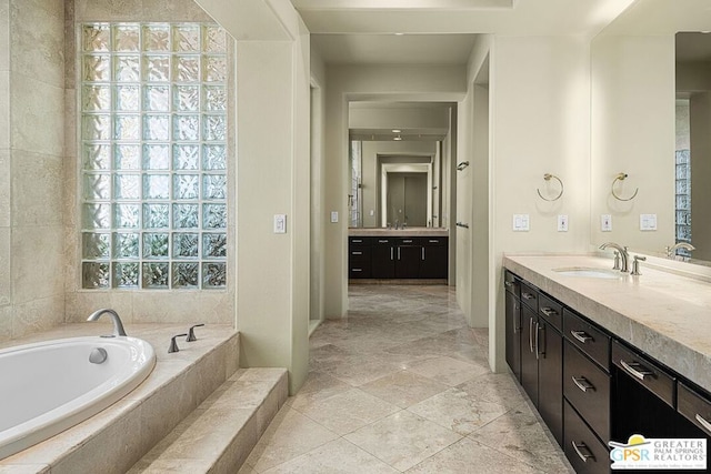 bathroom with a relaxing tiled tub, vanity, and plenty of natural light