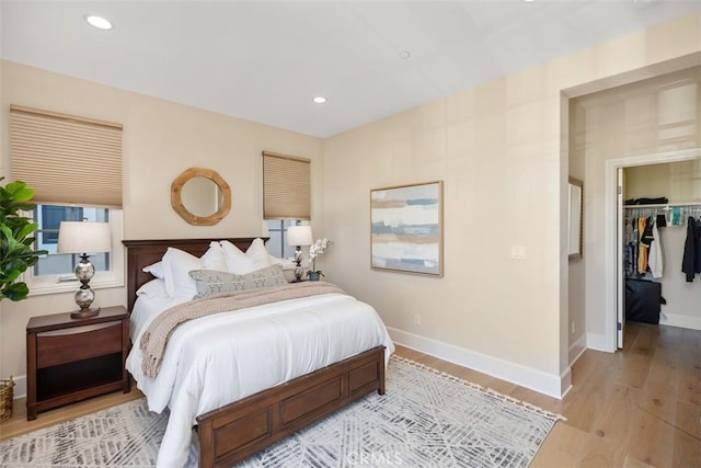 bedroom with recessed lighting, baseboards, light wood-style floors, a closet, and a walk in closet