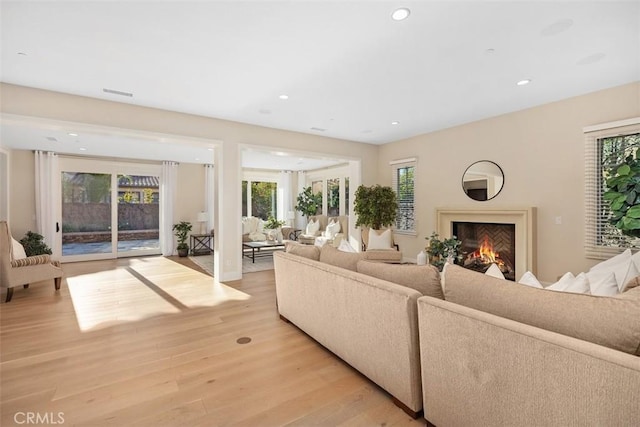 living room with recessed lighting, light wood-style flooring, visible vents, and a lit fireplace