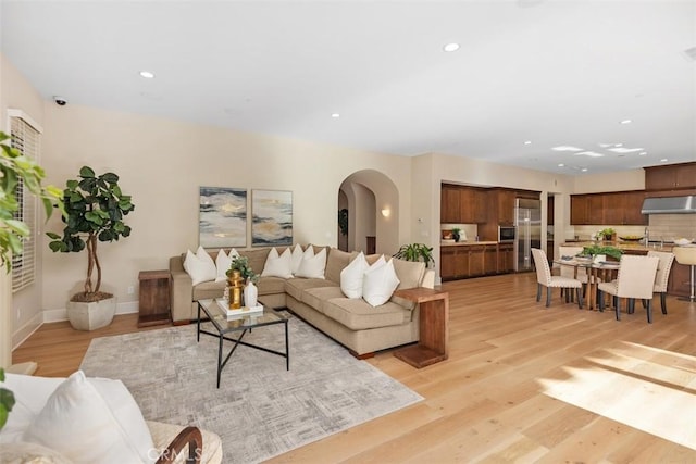 living room featuring light wood finished floors, baseboards, arched walkways, and recessed lighting