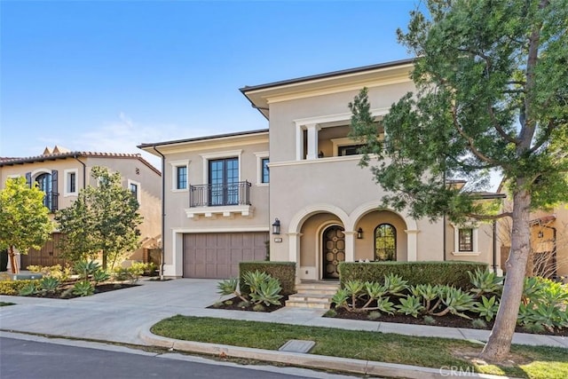 view of front facade featuring french doors, stucco siding, a balcony, a garage, and driveway