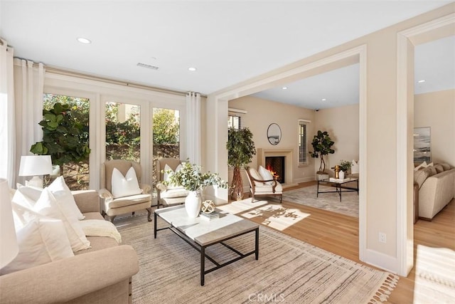 living room featuring recessed lighting, visible vents, light wood-style floors, a lit fireplace, and baseboards