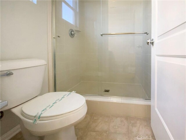 bathroom featuring a shower with door, tile patterned flooring, and toilet