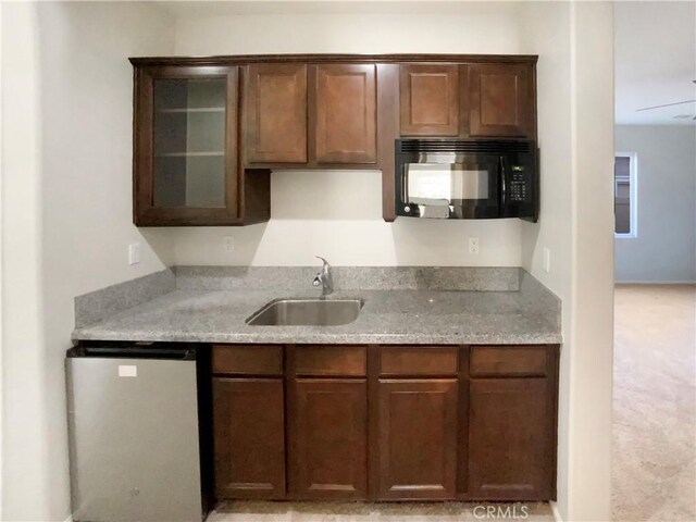 kitchen with light stone countertops, dark brown cabinetry, dishwashing machine, and sink