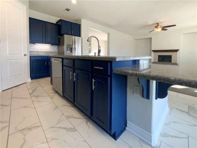 kitchen featuring tasteful backsplash, stainless steel appliances, blue cabinets, and a center island with sink