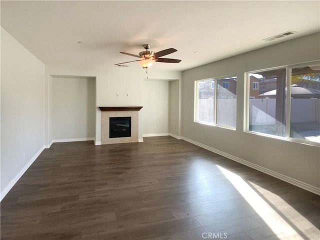 unfurnished living room with a tiled fireplace, dark wood-type flooring, and ceiling fan