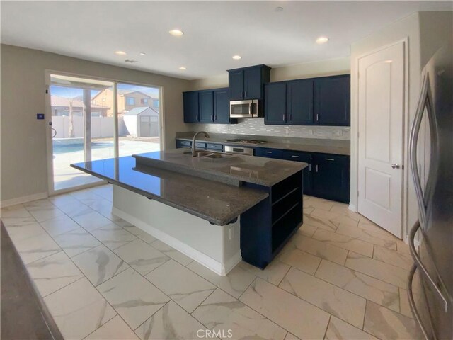 kitchen featuring an island with sink, decorative backsplash, blue cabinetry, appliances with stainless steel finishes, and sink