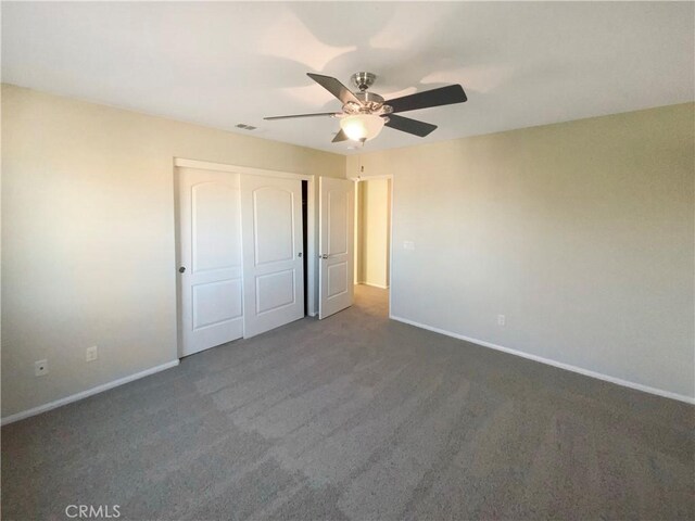 unfurnished bedroom featuring ceiling fan, a closet, and dark colored carpet