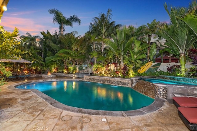 pool at dusk featuring an in ground hot tub and a patio area