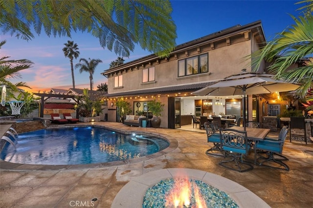 pool at dusk with pool water feature, a patio area, a pergola, and a fire pit