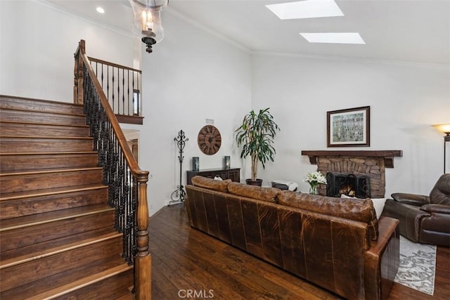 living room featuring dark hardwood / wood-style flooring, crown molding, lofted ceiling with skylight, and a stone fireplace