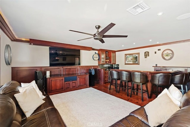 living room with ceiling fan, dark hardwood / wood-style floors, ornamental molding, and indoor bar