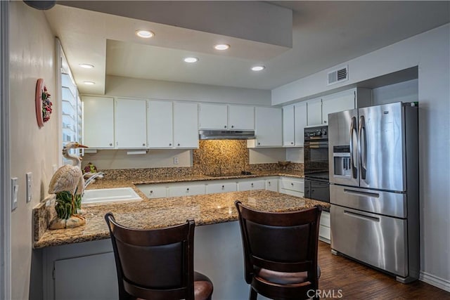 kitchen with a breakfast bar, stainless steel fridge, white cabinetry, and sink