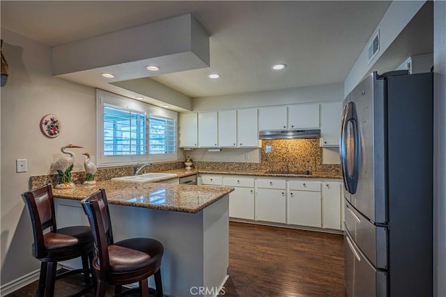 kitchen featuring kitchen peninsula, stainless steel fridge, white cabinetry, and a breakfast bar area