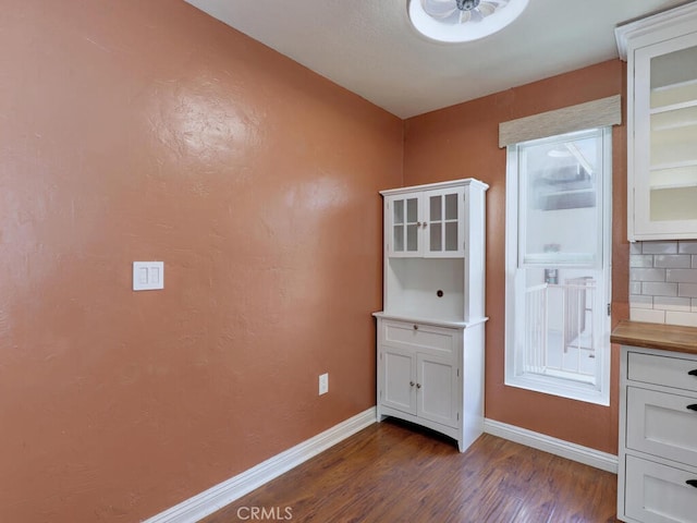 interior space featuring dark wood-type flooring, butcher block counters, decorative backsplash, and white cabinetry