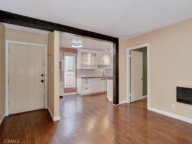 unfurnished living room with a textured ceiling, dark hardwood / wood-style floors, heating unit, beamed ceiling, and sink