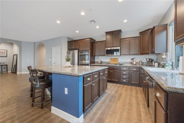 kitchen featuring appliances with stainless steel finishes, a center island, light stone counters, and sink