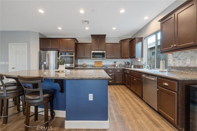 kitchen with stone counters, light wood-type flooring, decorative backsplash, a kitchen island, and appliances with stainless steel finishes