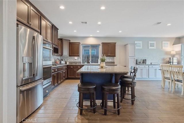 kitchen with stainless steel appliances, a center island, a breakfast bar, light stone counters, and dark brown cabinetry