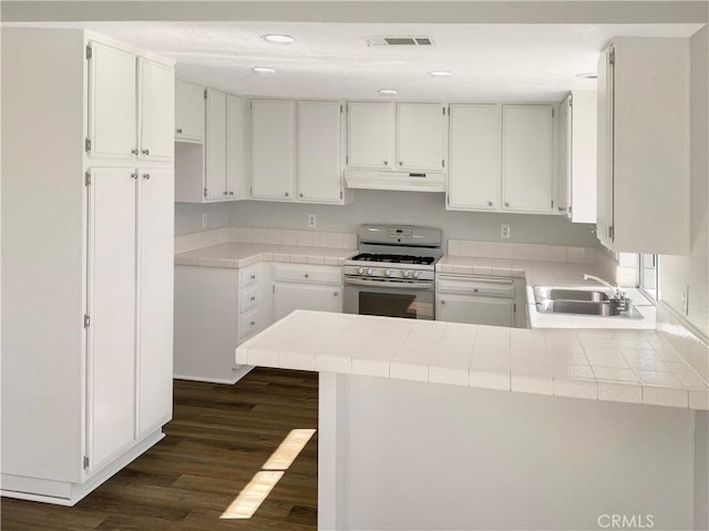 kitchen with sink, white cabinets, white gas range oven, kitchen peninsula, and tile counters