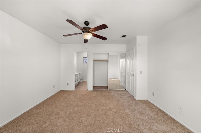 unfurnished bedroom featuring ensuite bathroom, light colored carpet, a ceiling fan, visible vents, and a closet