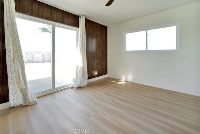 empty room featuring light wood-type flooring, wood walls, and ceiling fan