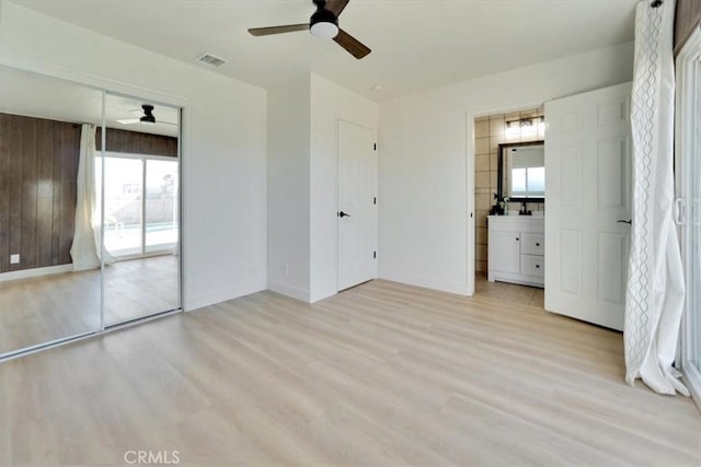 unfurnished bedroom featuring a closet, ensuite bathroom, ceiling fan, light hardwood / wood-style flooring, and access to outside