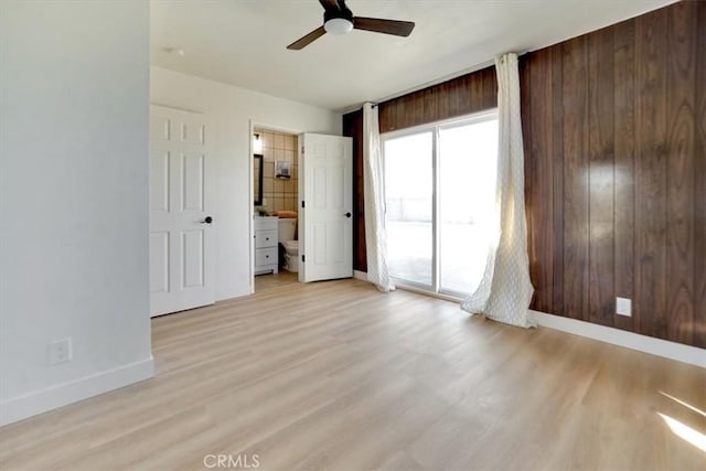 unfurnished bedroom with wooden walls, access to exterior, ceiling fan, light hardwood / wood-style floors, and ensuite bath