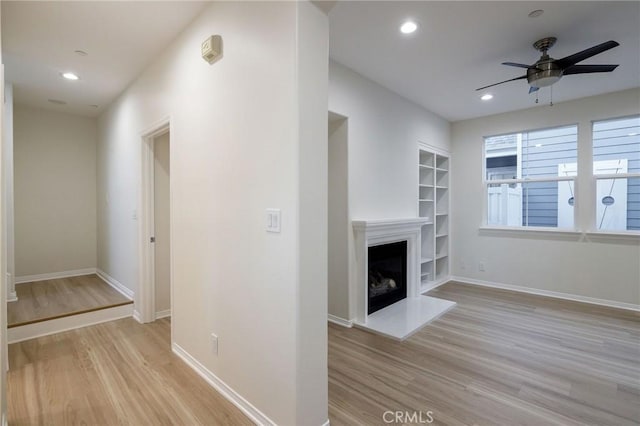 unfurnished living room with built in features, ceiling fan, and light hardwood / wood-style floors