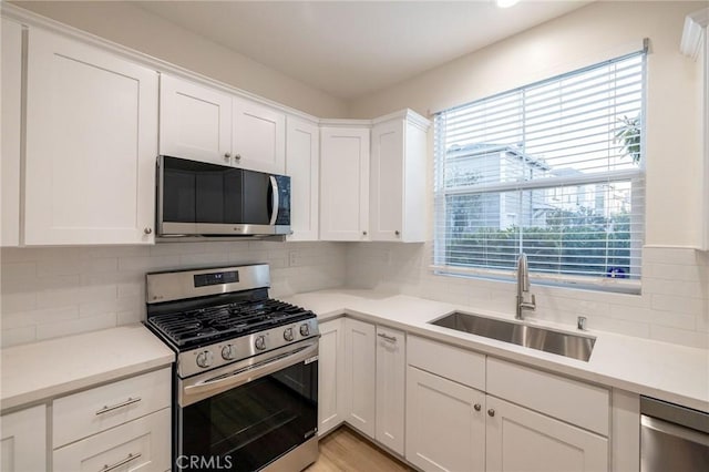 kitchen featuring appliances with stainless steel finishes, white cabinetry, decorative backsplash, and sink