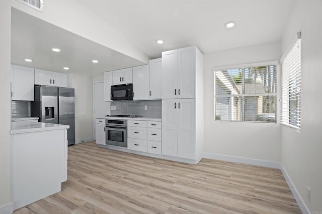 kitchen with vaulted ceiling, light hardwood / wood-style flooring, backsplash, white cabinets, and appliances with stainless steel finishes