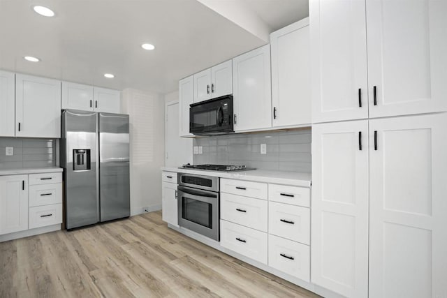 kitchen with white cabinets, stainless steel appliances, light hardwood / wood-style floors, and decorative backsplash