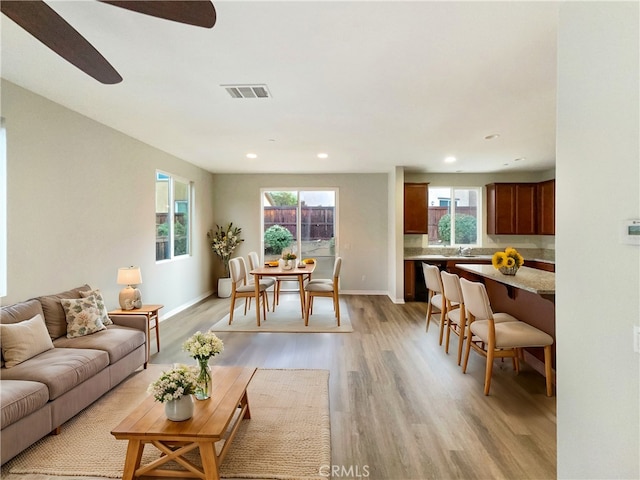 living room featuring sink, ceiling fan, light wood-type flooring, and a healthy amount of sunlight