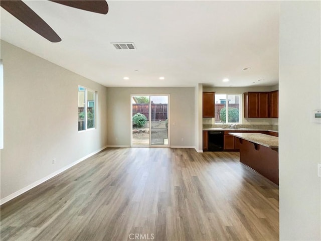 unfurnished living room featuring sink, light wood-type flooring, and a healthy amount of sunlight