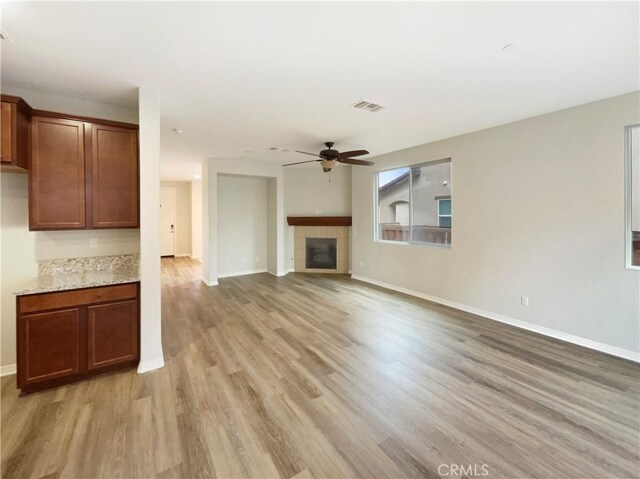 unfurnished living room with a tiled fireplace, light hardwood / wood-style floors, and ceiling fan