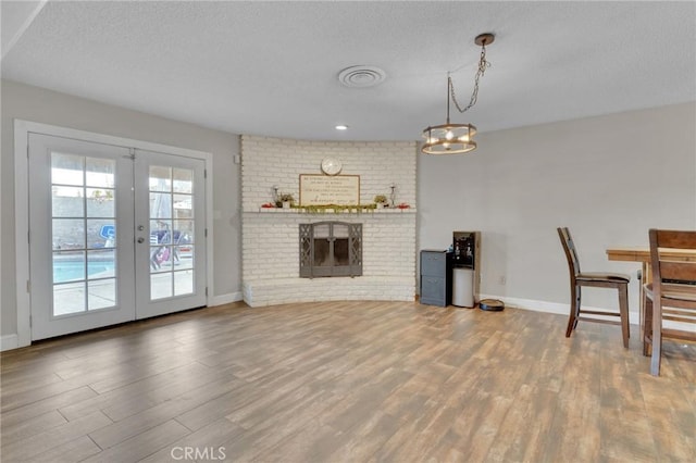 interior space featuring french doors, a brick fireplace, hardwood / wood-style flooring, a textured ceiling, and an inviting chandelier